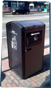 A street corner with a garbage can that is a solar compactor