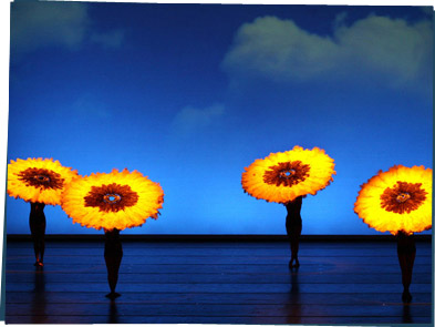 Dancers on stage holding giant flower heads to look like daisies.