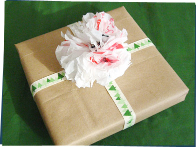 A present wrapped in a paper bag with a pompom made of plastic bags.